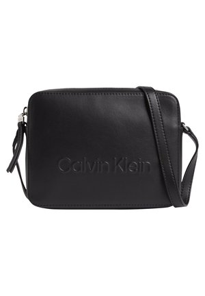 Czarna, prostokątna skórzana torba na ramię z tłoczonym "Calvin Klein" na przodzie i regulowanym paskiem na ramię.