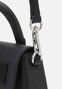 Black leather handbag featuring a textured finish, adjustable strap, and a silver metal clasp with brand engraving. Sharp rectangular accents.