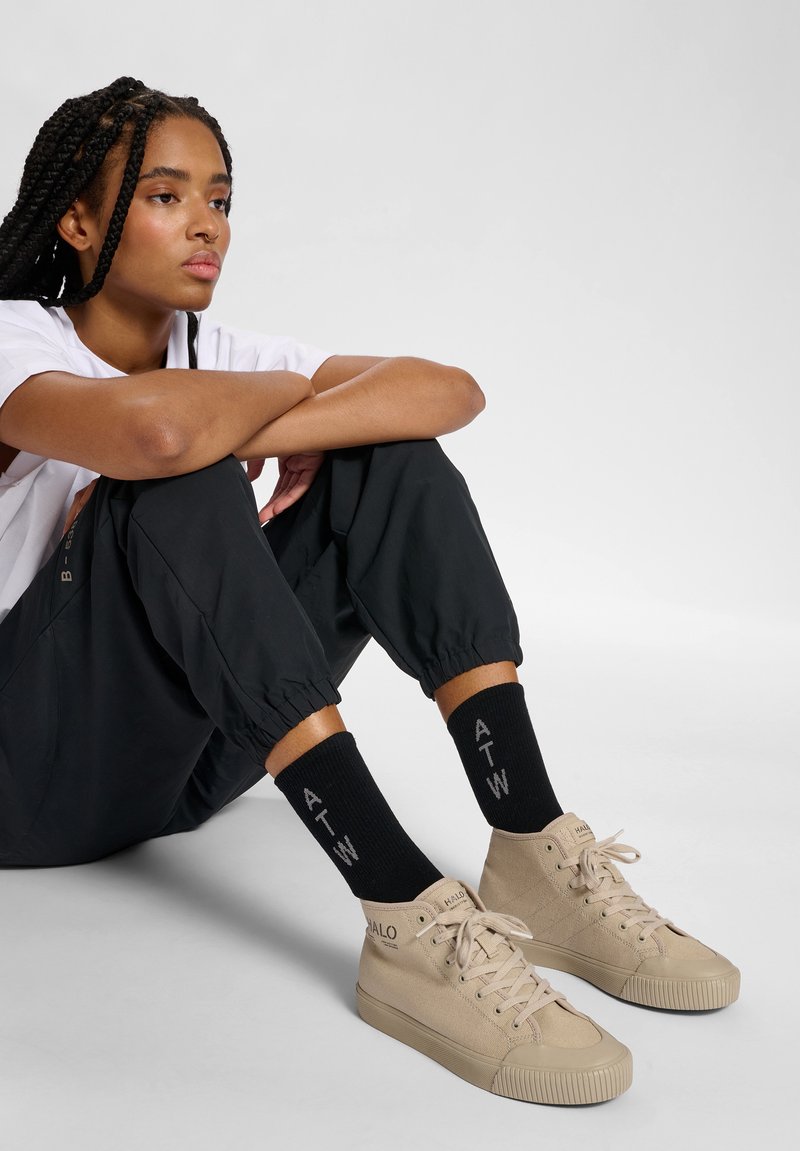 Tanowe trampki wysokie z teksturowanym płótnem, w zestawie z czarnymi skarpetkami ribbed z białym napisem "ATW" oraz luźnymi czarnymi spodniami.
