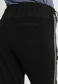 Zwarte sportbroek met een elastische tailleband, gestructureerde stof en een zilveren zijstreep. Beschikt over een achterzak en heeft een comfortabele pasvorm.