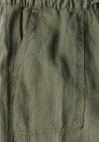 Olivgrön cargoshorts tillverkade av lätt tyg, med elastisk midja och sidofickor med synliga sömdekorationer.