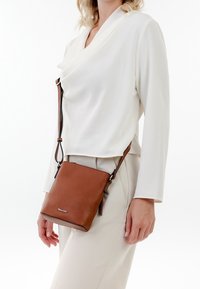 Brun lær crossbody taske med justerbar strap, rektangulær form, glat tekstur og sølv logo detalje på fronten.