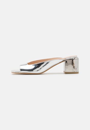 Mule con tacco a blocco open-toe in argento metallico. Superficie liscia e riflettente; design minimalista con silhouette curva.