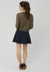 Pull brun texturé associé à une jupe évasée bleu marine avec des éclats dorés. Le modèle porte des chaussures brunes avec des chaussettes bordeaux et un chouchou à pois.