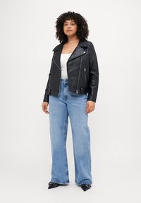 Melnā mākslīgās ādas motokreklā ar sudraba zipa, pieguļošs dizains un plati kluči, kombinēts ar gaiši ziliem augsto vidukli džinsiem.