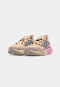 Running shoes in beige mesh with pink and grey accents. Features textured sole, lace-up design, and branding on the tongue and sides.