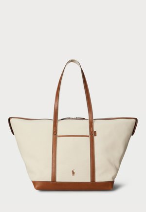 Beige lerret tote bag med brune skinndetaljer, to skulderremmer, en frontlomme og brodert logo foran. Glidelås lukking på toppen.