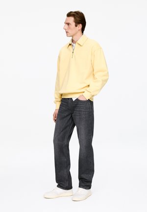Light yellow zip-up sweater, gray jeans, and white sneakers. Sweater features a collar and relaxed fit, with denim having a slightly textured finish.