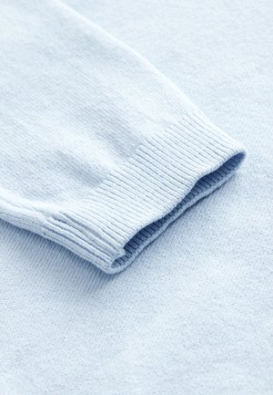 Světle modrý svetr zblízka, ukazující měkkou texturu, žebrované manžety a hladký povrch látky.
