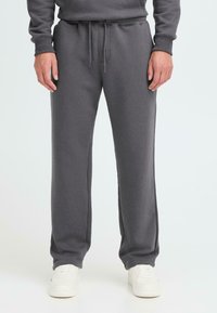 Grå sweatpants med snøre i taljen, tapered ben og en blød tekstur, parret med hvide træningssko.