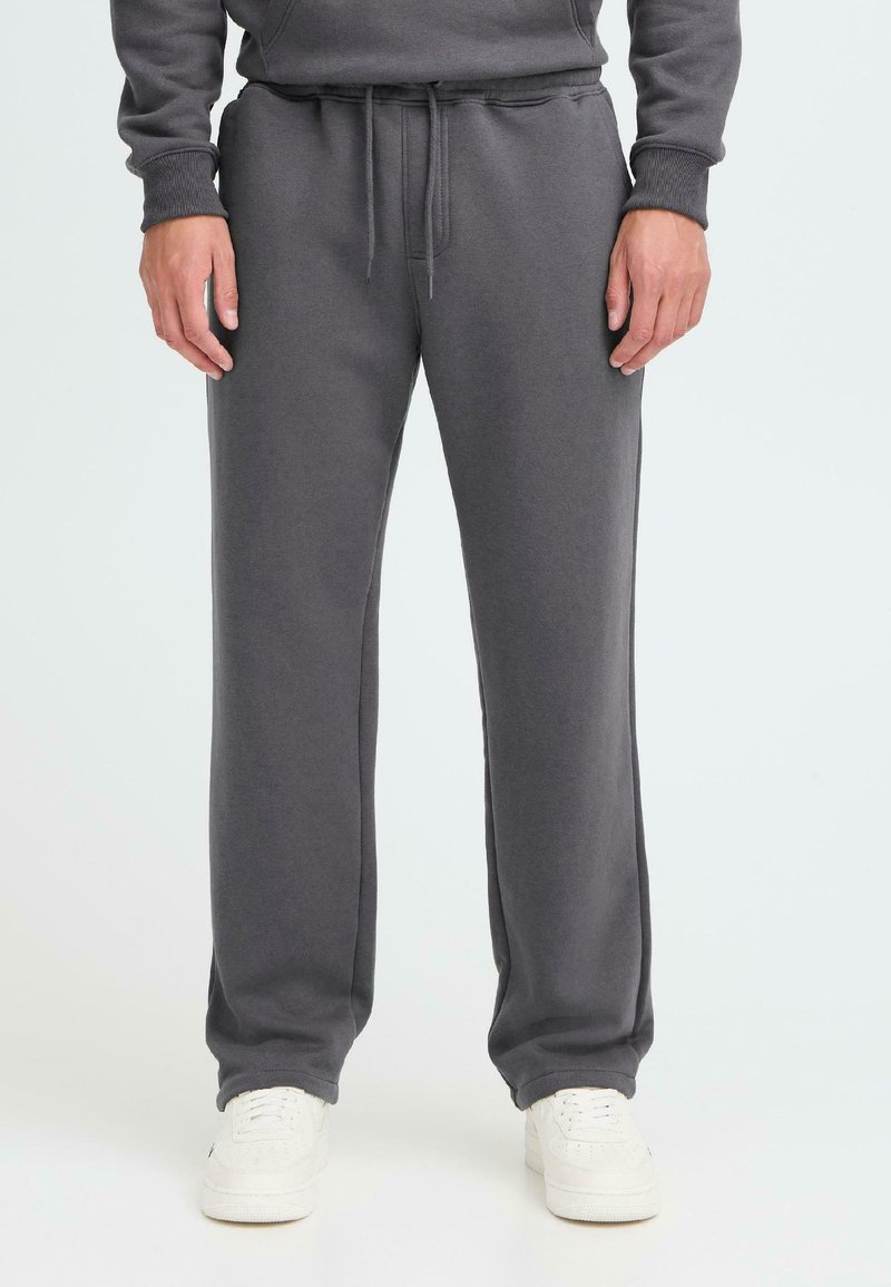 Grå sweatpants med snøre i taljen, tapered ben og en blød tekstur, parret med hvide træningssko.