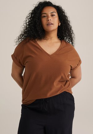 Brown v-neck T-shirt with rolled sleeves, textured fabric, and a relaxed fit. Paired with dark, loose-fitting pants.