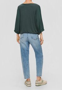 Top verde con mangas anchas, combinado con jeans azul claro ajustados y zapatillas beige. Tela suave y ajuste relajado.