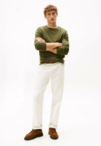 Maglione verde, jeans bianchi e scarpe in suede marroni. Il maglione ha un collo tondo e polsini a coste, mentre i jeans hanno una vestibilità dritta.