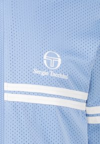 Giacca a rete blu chiaro con strisce orizzontali bianche e un piccolo logo. Il tessuto è traspirante e presenta una texture perforata.