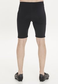 Schwarze Radsportshorts mit enger Passform und gepolstertem Sitzbereich, ausgestattet mit einer glatten Textur und einem elastischen Bund, kombiniert mit schwarzen Radschuhen.