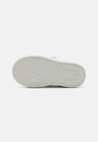 Semelle de sneaker blanche avec une surface texturée, présentant un logo circulaire et un motif de semelle pour adhérence et traction.
