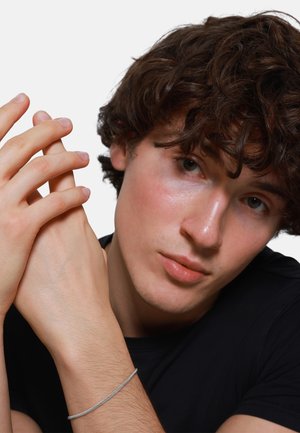 Silver bracelet on wrist, short curly brown hair, fair skin, wearing a black shirt. Hands clasped, fingers gently positioned.