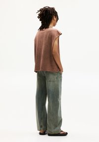 Un haut sans manches oversize marron associé à un jean large délavé bleu. Le tissu semble doux, avec une coupe décontractée et des détails de couture minimalistes.