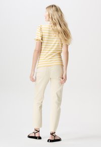 Gul och vit randig kortärmad topp i kombination med ljusbeiga byxor, som visar upp en figurnära design och böjd nederkant. Svarta sandaletter med remmar fulländar looken.