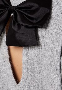 Pull gris texturé avec une découpe en V profonde, agrémentée d'un grand nœud en satin noir au niveau du col.