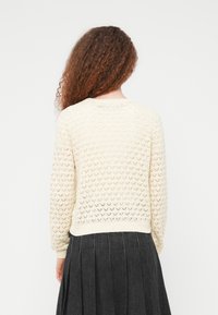 Πλεκτό πουλόβερ  σε ανοιχτό κρεμ χρώμα με υφή και διάτρητο σχέδιο, καθώς και ριμπ μανσέτες. Η πλάτη έχει στρογγυλεμένο λαιμόκοψη και άνετη εφαρμογή.