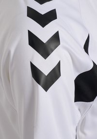 Tissu blanc avec quatre flèches chevrons noires pointant vers le bas, disposées verticalement sur la manche.