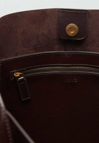 Interno di una borsa a mano in cuoio marrone con una superficie liscia, dotato di una tasca con zip e una chiusura a scatto magnetico. Presenti dettagli in hardware color oro.