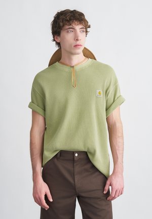 Tricou scurt cu mâneci scurte, verde deschis, cu dungi, cu decolteu rotund și manșete întoarse, având o mică emblemă și un detaliu din șnur maro deschis.