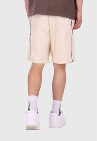 Leichte Cremeshorts mit lockerer Passform, ausgestattet mit einem kontrastierenden dunklen Seitenstreifen und einem elastischen Taillenbund, kombiniert mit weißen Sneakers.