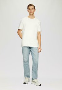 Camiseta blanca de algodón, de mangas cortas, combinada con jeans de mezclilla azul claro. Los zapatos son de un gris claro con detalles en negro y un diseño texturizado.