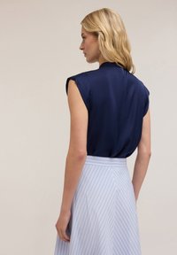 Blusa senza maniche blu navy con colletto alto, abbinata a una gonna azzurra chiara con strisce bianche verticali. Tessuto morbido, vestibilità comoda.