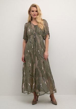 Grön blommig maxiklänning med svängande ärmar, knappdetaljer fram och transparent textur. Matchas med beige högklackade skor.