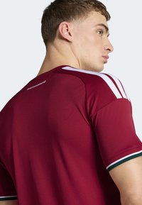 Vinrød atletisk skjorte med hvide skulderstriber, korte ærmer og manschetter med grønne accenter. Fremstillet af glat, let stof.