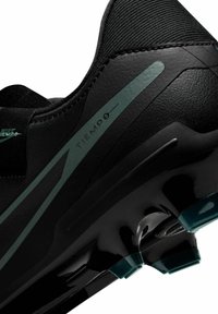 Black soccer cleat with a textured upper, featuring a green accent stripe, rounded toe, and a glossy black sole with blue studs.