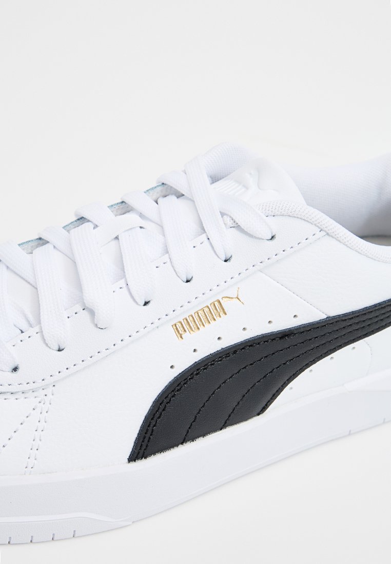Sneaker in pelle bianca con accenti neri, suola piatta e logo dorato. Presenta punta rotonda, design con lacci e dettagli cuciti.