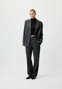 Costume gris à rayures avec une veste croisée et un pantalon sur mesure. Un col roulé noir en dessous. Des chaussures en cuir complètent le look.
