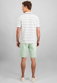 Prugasta polo majica u bijeloj i tamnoplavoj boji, u kombinaciji s kratkim hlačama u boji mente. Outfit sadrži klasičan ovratnik i opušteni kroj, pogodan za ležerno nošenje.