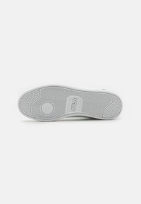 Suela de zapatilla de goma blanca con patrones texturizados, acento de logotipo circular y distintivo dibujo de espiga para mayor agarre.