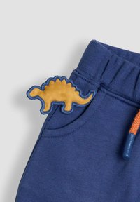 Námornícke modré tepláky s textúrovanou oranžovou nálepkou dinosaura na vrecku, s ribbovaným pásom a oranžovým šnúrkou.