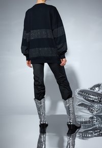Svart oversized sweatshirt med vita prickiga detaljer, tillsammans med svarta byxor och silverfärgade cowboyboots med dekorativa mönster.