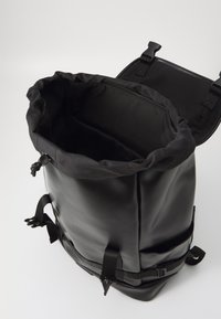 Zaino nero con coulisse in materiale impermeabile, spallacci regolabili e apertura a sacco. Caratterizzato da una superficie liscia e da un design minimalista.