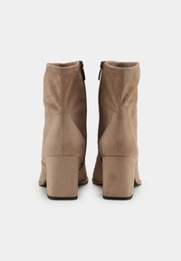 Beige suede ankle boots with a block heel, featuring a side zipper and stitched detailing along the back seam. Smooth texture, versatile design.