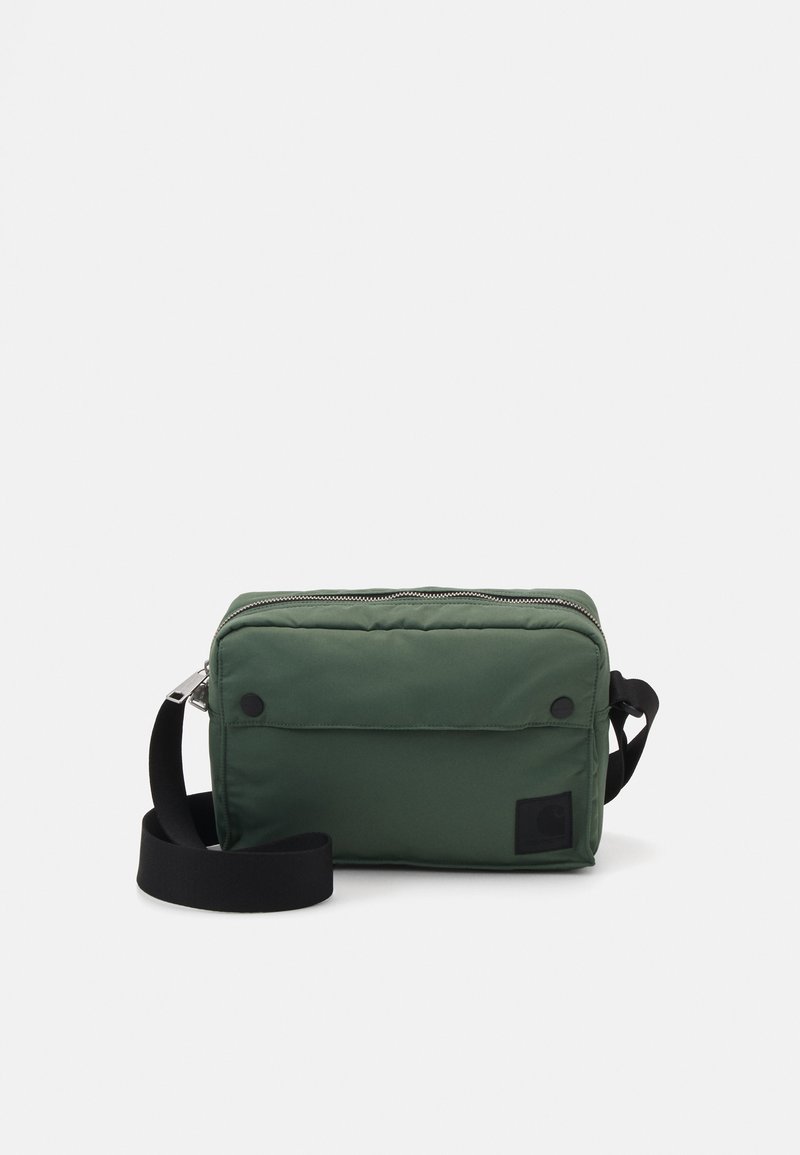 Grøn nylon crossbody taske med lynlåslukning, justerbar sort rem, frontlomme og et logo-patch på siden. Glat tekstur.