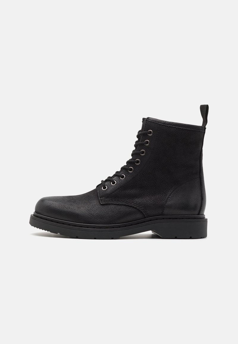 Botte de combat noire à lacets avec finition en cuir texturé, semelle robuste et languette à l'arrière du talon, montrée de profil sur fond blanc.