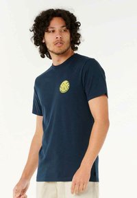 Marineblå bomulds t-shirt med et rundt gult logo på venstre bryst, rund halsudskæring og korte ærmer. Glat tekstur, afslappet pasform.