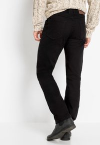 Pantaloni neri con una vestibilità slim, realizzati in un tessuto morbido. Presentano tasche posteriori con dettagli cuciti e una patch in pelle sul cinturino.