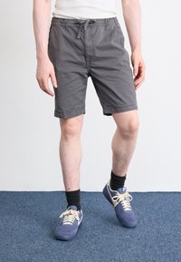 Shorts en coton gris avec une taille élastique et un cordon de serrage, dotés de deux poches latérales. Portés avec des baskets navy et des chaussettes noires.