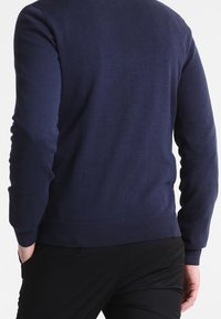 Marinblå tröja gjord av stickat tyg. Har en rund halsringning, ribbade ärmslut och fåll. Bakvy med slät textur och figurnära design.