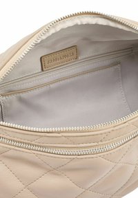 Interno di borsa in pelle beige con motivo trapuntato a diamante, dotata di un compartimento con cerniera e un'etichetta decorativa, fodera liscia in raso.